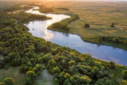Aerial view of a winding river surrounded by lush greenery and open fields at sunset.