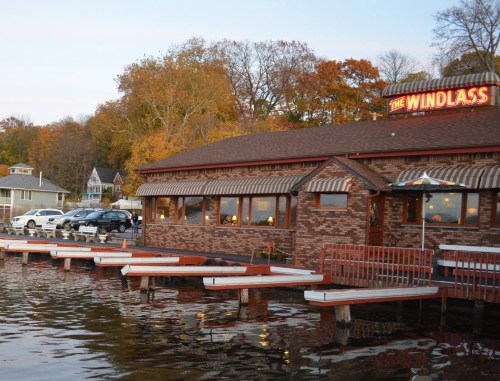 A lakeside restaurant named "The Windlass" with a brick exterior and boats docked nearby, surrounded by autumn trees.