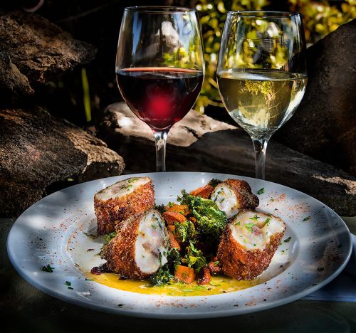 A plate of crispy stuffed rolls with greens and vegetables, accompanied by glasses of red and white wine.