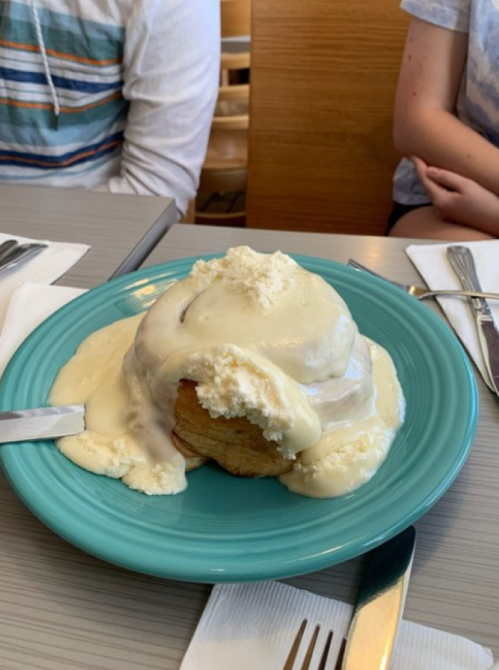 A large biscuit topped with creamy sauce and ice cream, served on a turquoise plate at a dining table.