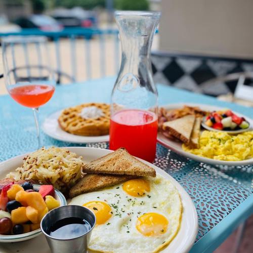 A colorful brunch spread featuring eggs, toast, hash browns, fruit salad, waffles, and drinks on a blue table.