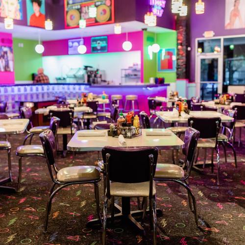 A colorful diner interior with retro decor, featuring tables, chairs, and a vibrant atmosphere.