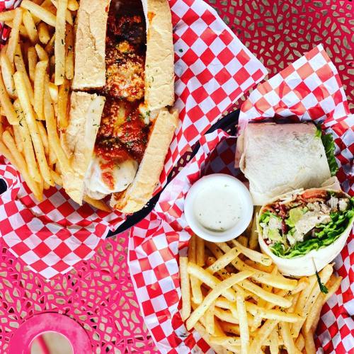 A vibrant table with a sandwich, fries, and a wrap served with a dipping sauce in a red-checkered basket.