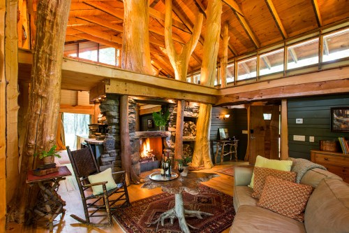 Cozy cabin interior with wooden beams, a stone fireplace, and rustic furniture, surrounded by nature.