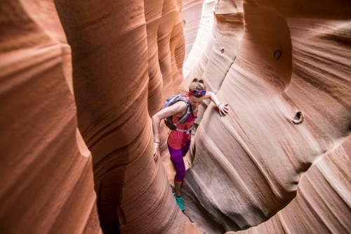A person navigating through a narrow, winding canyon with smooth, colorful rock formations.