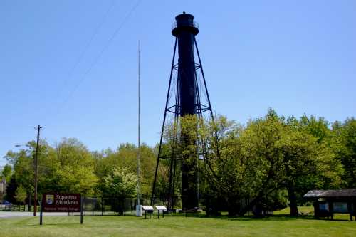 A tall black lighthouse stands among green trees under a clear blue sky at Supawna Meadows National Wildlife Refuge.