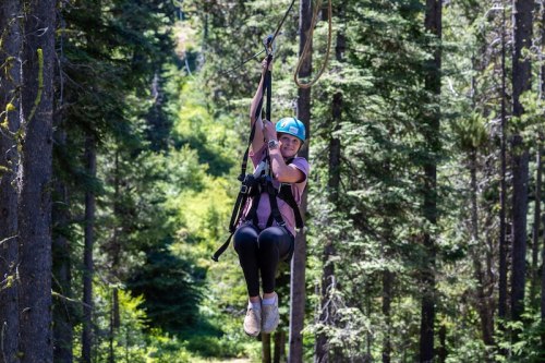 A person zip-lining through a lush green forest, smiling and enjoying the adventure.