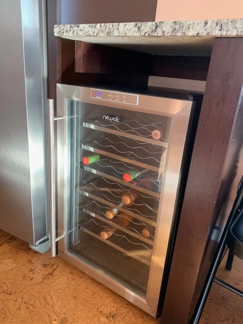 A wine cooler with several bottles displayed, set under a countertop in a kitchen.