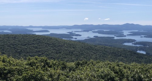 A panoramic view of lush green hills and a serene lake dotted with islands under a clear blue sky.