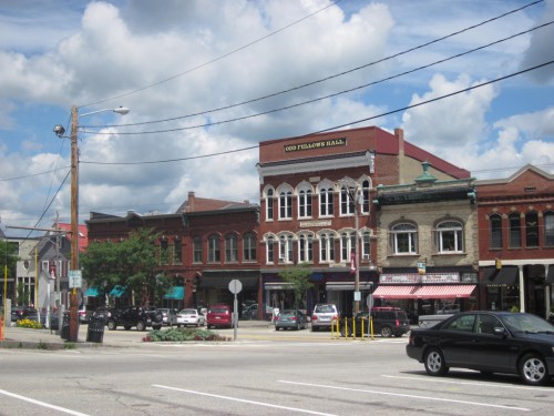 A charming street scene featuring historic buildings, shops, and a blue sky with fluffy clouds.