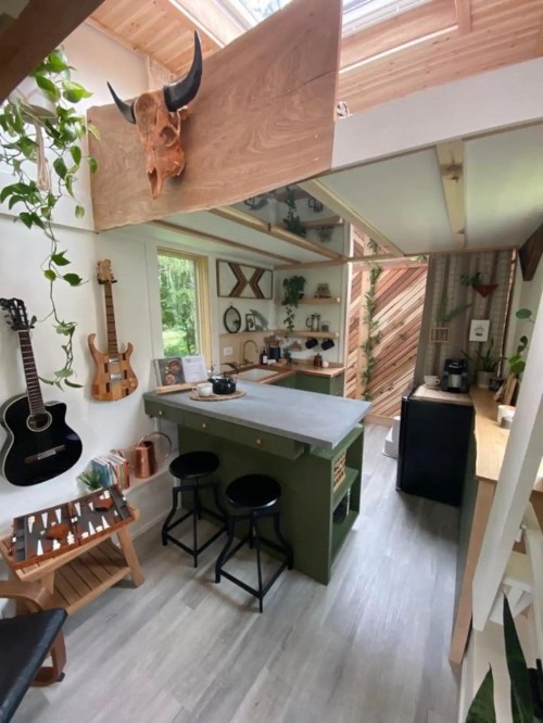 Cozy kitchen with a concrete island, wooden accents, plants, and musical instruments, featuring natural light from skylights.