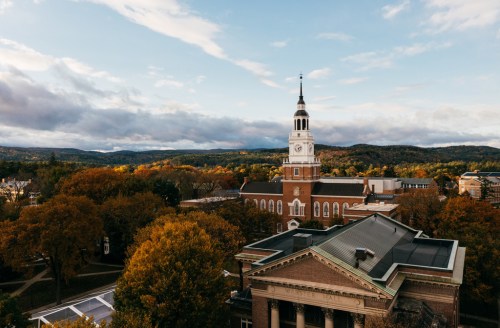 Aerial view of a historic building with a clock tower, surrounded by autumn trees and mountains in the background.