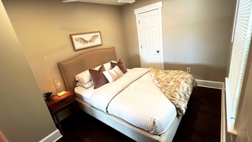 Cozy bedroom featuring a bed with decorative pillows, a bedside table, and soft lighting. Warm, neutral tones throughout.
