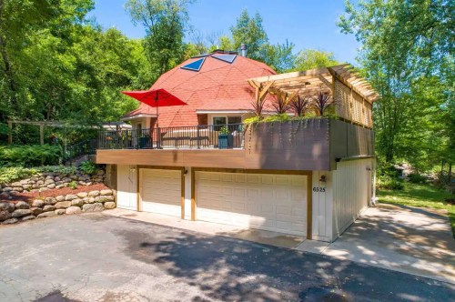 A unique dome-shaped house with a deck, surrounded by trees and a stone pathway, featuring a red umbrella on the patio.