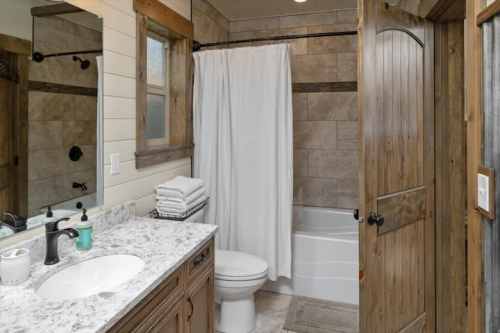 A cozy bathroom featuring a tub, shower curtain, sink with countertop, and wooden accents.