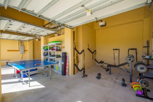 A spacious garage with a ping pong table, exercise equipment, and storage shelves against the walls.