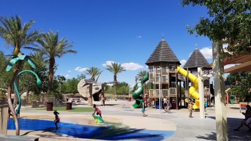 A vibrant playground with slides, palm trees, and children playing in a sunny outdoor setting.