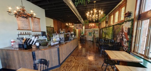 Cozy café interior with wooden tables, a long counter, and decorative wall murals of nature and whimsical scenes.