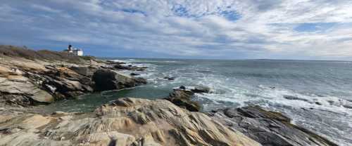 A rocky coastline with waves crashing, under a cloudy sky, featuring a distant lighthouse on a cliff.