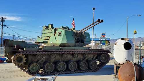 A military tank parked near a gas station, with a large white object nearby and clear blue skies above.