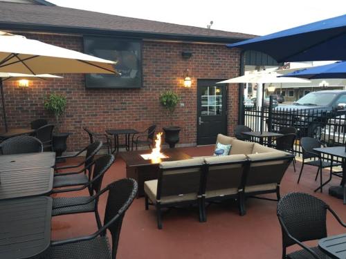Outdoor patio with seating, umbrellas, and a fire pit, featuring a brick wall and a large screen in the background.
