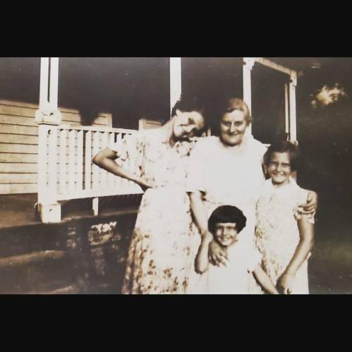 A vintage photo of four women, including a grandmother and three girls, smiling together on a porch.