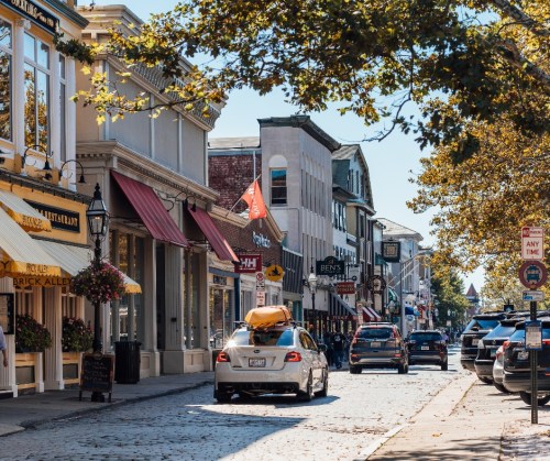 A charming street lined with shops and restaurants, featuring a car and trees under a clear blue sky.