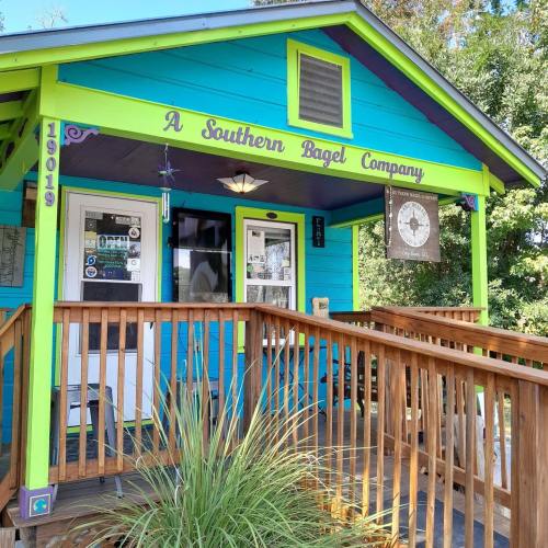 Colorful exterior of "A Southern Bagel Company" with a wooden deck and vibrant blue and green walls.