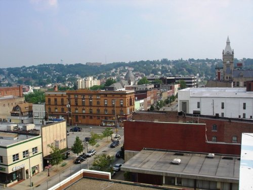 A panoramic view of a small town with buildings, trees, and a clock tower in the distance under a clear sky.