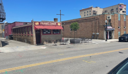 A street view of Frank's Diner, featuring outdoor seating and nearby brick buildings under a clear blue sky.