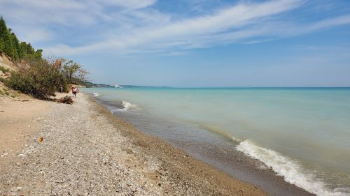 A serene beach scene with a pebbly shore, gentle waves, and a clear blue sky in the background.