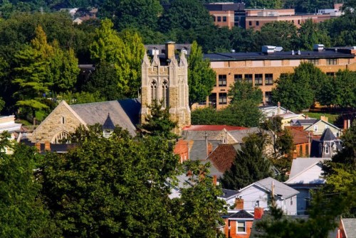 A scenic view of a town with a church tower surrounded by trees and buildings in the background.
