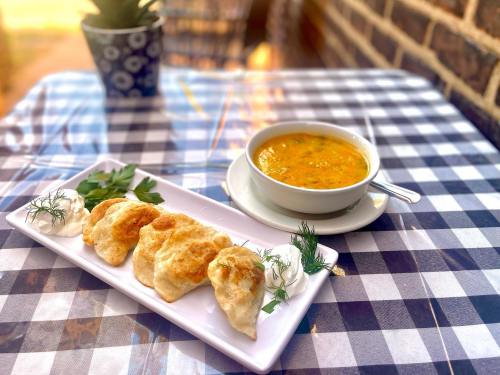 A plate of golden pastries with herbs and sour cream, alongside a bowl of soup, on a checkered tablecloth.
