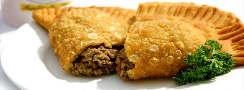 A plate of golden-brown empanadas, one cut open to reveal a savory meat filling, garnished with parsley.