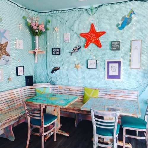 Cozy café interior with turquoise walls, wooden seating, nautical decor, and fairy lights creating a whimsical atmosphere.