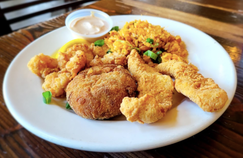 A plate of fried seafood, including fish fillets, shrimp, a crab cake, and seasoned rice, served with a dipping sauce.