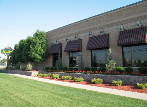 Exterior view of a restaurant with striped awnings, landscaped garden, and a sign reading "Mallie’s."