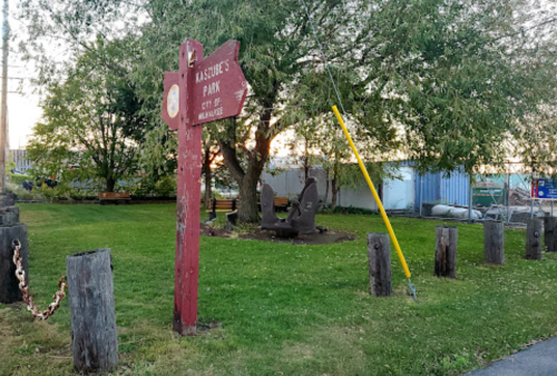 A park sign points to "Rascal's Park" with grassy areas, trees, and a few sculptures in the background.