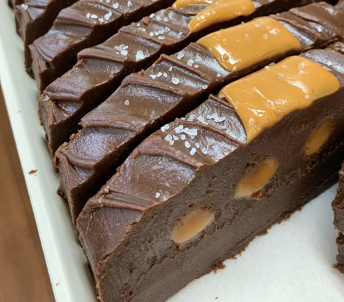 Close-up of chocolate fudge slices topped with caramel and sprinkled with sea salt, showcasing a rich, creamy texture.