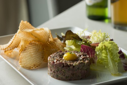 A plate featuring beef tartare topped with an egg yolk, accompanied by crispy chips and a fresh salad.