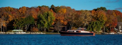 A boat floats on a lake surrounded by vibrant autumn foliage and a clear blue sky.