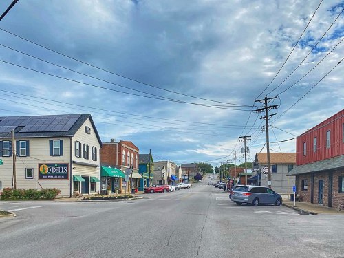 A small town street lined with shops and buildings under a cloudy sky, with power lines overhead.