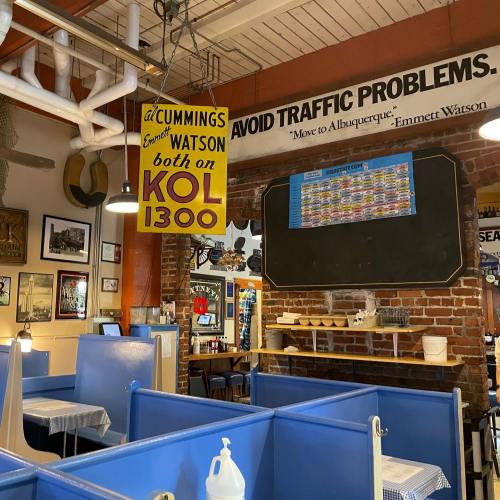 Interior of a restaurant featuring blue booths, vintage decor, and a sign about traffic problems and a radio station.