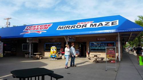 Exterior of a building with a blue awning labeled "Krazy Mirror Maze" and "Torture Museum," featuring colorful signage.