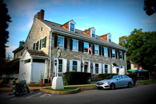 Historic stone building with green shutters, an American flag, and parked cars in front on a sunny day.