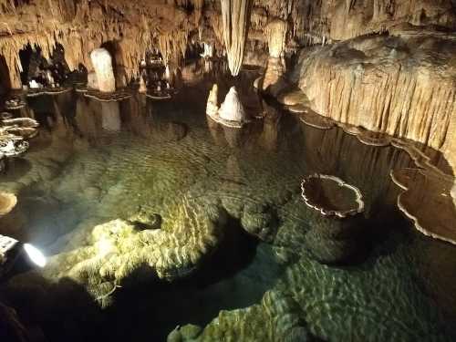 A serene underground cave with stalactites and stalagmites reflected in clear water.