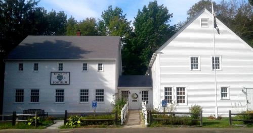 Two white buildings with a sign reading "Town of Foster, RI," surrounded by greenery and a clear blue sky.