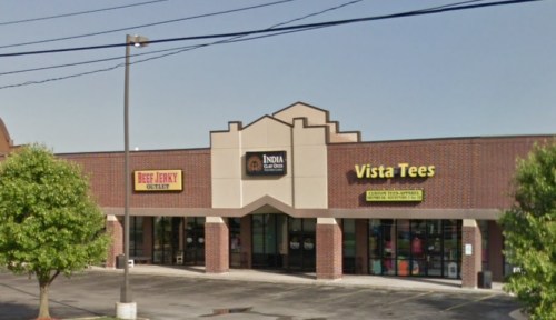 A storefront featuring Beef Jerky Outlet, India Grill, and Vista Tees, with trees and a clear blue sky in the background.