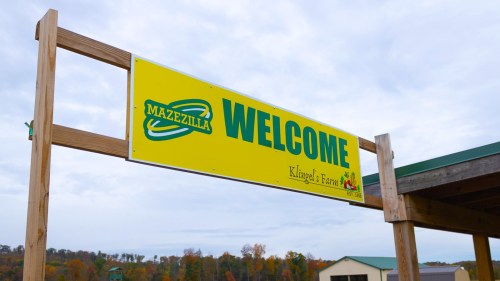 A large yellow sign reading "Welcome to Mazezilla" hangs on a wooden structure against a cloudy sky.