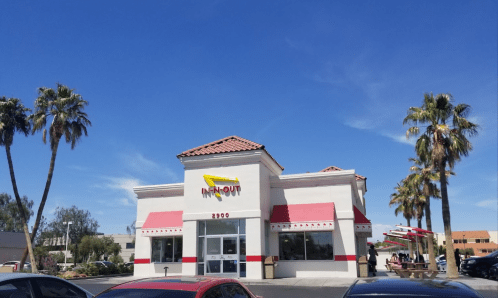 A bright In-N-Out Burger restaurant with palm trees and a clear blue sky in the background.